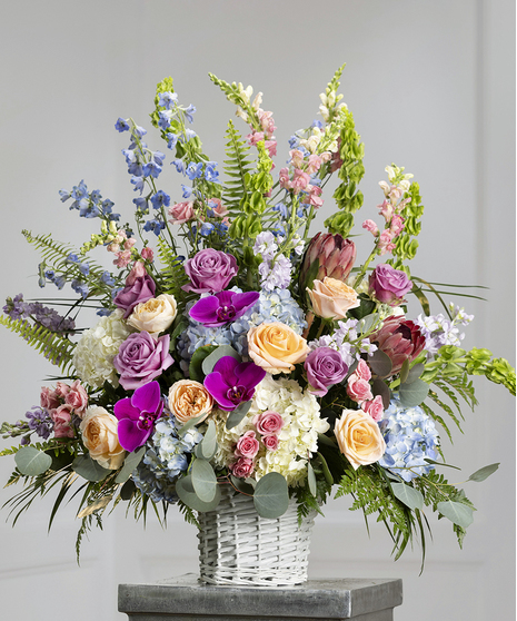 Pastel Garden Sympathy Basket featuring hydrangea, stock, snapdragons, delphinium, and orchids in a wicker basket