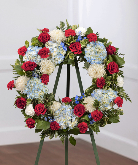 Patriot Garden Sympathy Wreath featuring hydrangea, roses, delphinium and foliage on a standing easel